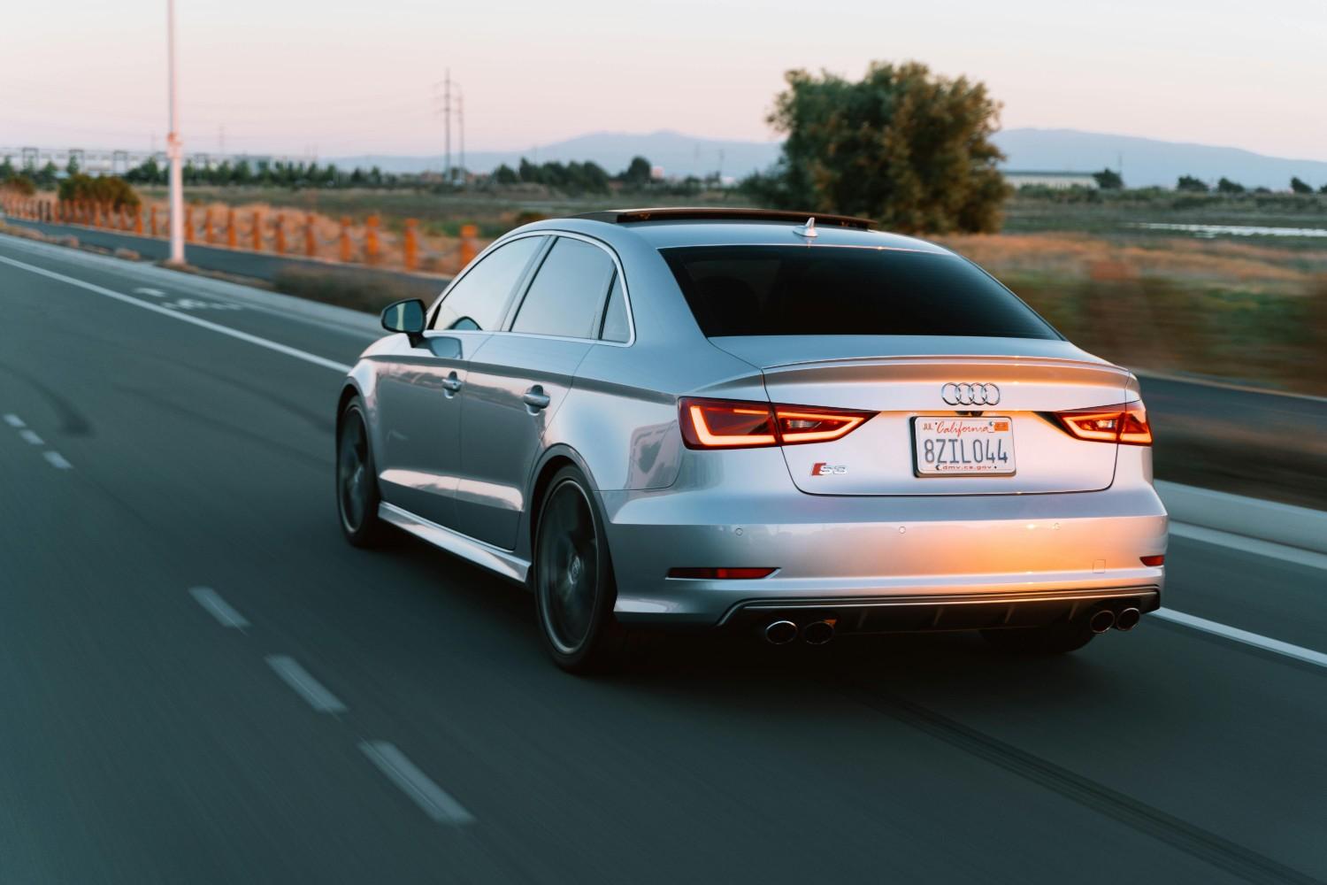 A modern silver sedan driving on a clean highway during sunset